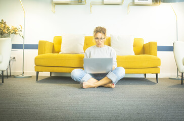 Young woman at home sitting on floor with crossed legs working or studying using laptop in the living room at home. Woman sitting on living room floor working on laptop at home office
