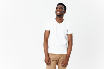 happy african man in white t-shirt and beige pants on light background cropped view