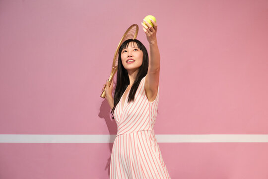 Young Asian Woman Pretending Playing Tennis Against Pastel Pink Background.