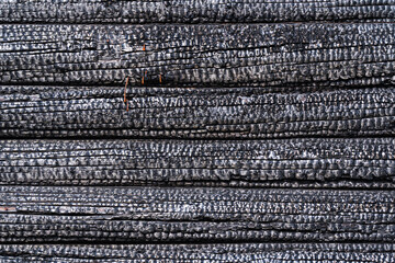 Burnt wall of a wooden house made of logs. The surface is covered with a black charred layer. Background. Texture.