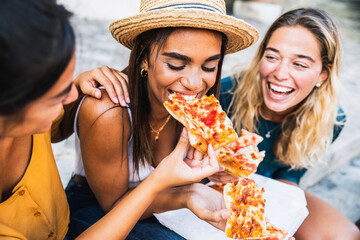 Three young female friends sitting outdoor and eating pizza - Happy women having fun enjoying a day...