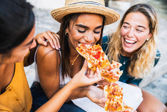 Fototapeta Three young female friends sitting outdoor and eating pizza - Happy women having fun enjoying a day out on city street - Happy lifestyle concept