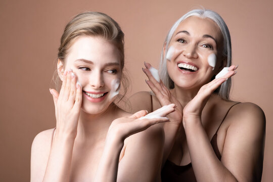 Joyful women young girl, mature gray-haired female applying foaming cleanser on cheeks for clean fresh healthy skin. Happy family washing faces by cleansing cosmetics product. Skincare routine