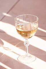 glass of white wine on tiles with shadows outdoor on terrace summer day