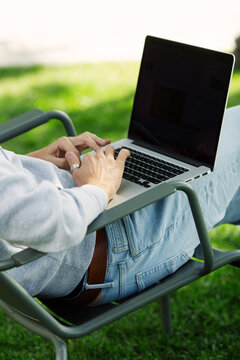 Freelancer man with laptop working outdoors in garden sitting on chair. Close up arms of programmer male work on computer in the park, typing on keyboard, rear view. Place of work, remote office