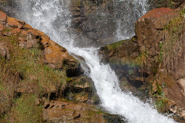 Close-up of a powerful waterfall in high quality. Side view of a sun-drenched waterfall in the wild. A large stream of water pours down from the mountain.