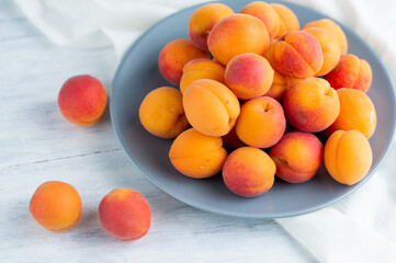 On a light background, a white plate with ripe, juicy apricots. Fruit background.