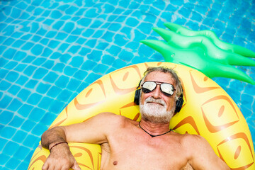 Closeup of caucasian senior man in the pool with headphones - obrazy, fototapety, plakaty