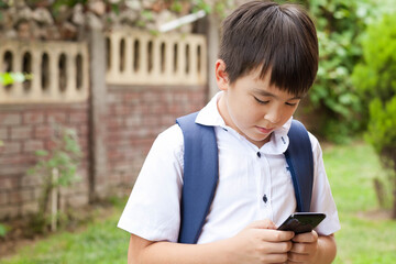 
Cute asian schoolboy boy writes a message on the phone outdoors. Communication and gadgets