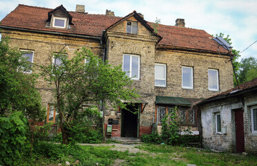 Fototapeta na wymiar Old brown brick building with red tile roof standing in greenery