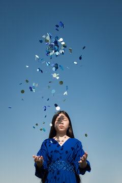 conceptual portrait of asian girl outside in bliue dress throwing glitter confetti in the air