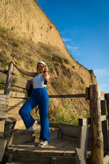 Naklejka premium Portrait of hiker cute teenage girl on the stairs going to the top of mountain. Traveling concept background. Woman traveler with backpack and bandana standing and looking on mountain hills.