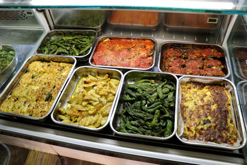 Typical Italian foods ready for purchase in an Italian take-away deli. Friggitelli, baked potatoes, vegetables au gratin, potato gateau, aubergine parmigiana