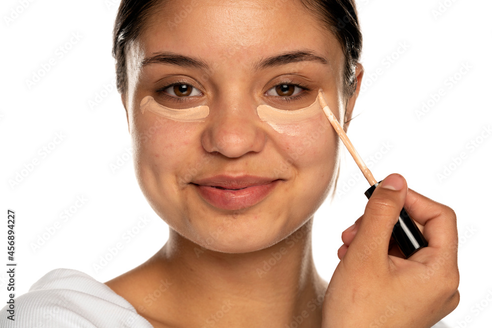 Wall mural closeup of a young beautifu smilingl woman applies concealer under her eye