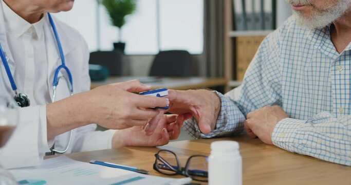 Close up of unknown professional female doctor which checking oxygen level in bearded patient using pusle oximeter during his visit to clinic