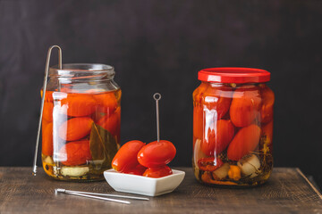 Pickled red cherry tomatoes in a glass jar on the old wooden background, selective focus