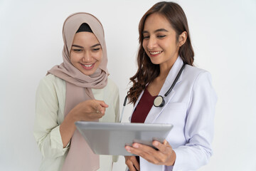 smiling veiled woman with pointing hand and happy beautiful female doctor while using tablet...