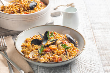 Seafood pasta. Fregula with seafood on a white wood surface. - obrazy, fototapety, plakaty