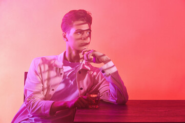 A man on an orange-purple background with a glass of whiskey