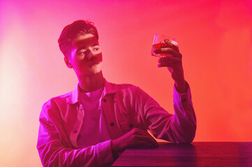 A man on an orange-purple background with a glass of whiskey