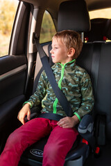 Little boy sitting on a booster seat buckled up in the car. - obrazy, fototapety, plakaty