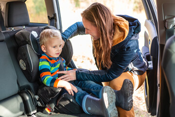 Mother fastening safety belt for her baby boy in his car seat.