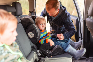 Father fastening safety belt for his baby boy in his car seat.