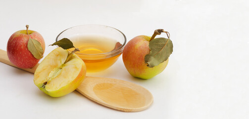 Two apples with leaves, a half of apple with green leaf, wooden spoon with apple cider vinegar and bowl with apple cider vinegar.