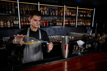 Bartender in apron adds ingredient to shaker