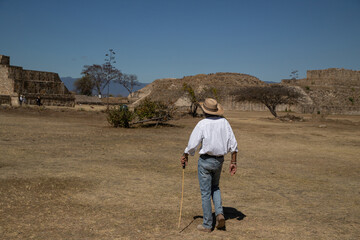 A man in a hat walks through an ancient city in Mexico. 