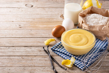 Pastry cream in a bowl and ingredients on wooden table. Copy space