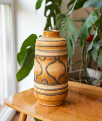 Mid-century modern pottery, brown vase on a wooden table with philodondendron in the background