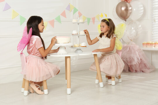 Cute little girls wearing fairy costumes at table with desserts in decorated room