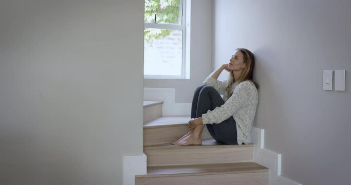 Sad young woman crying on step at home has a broken heart is overcome with grief and pain
