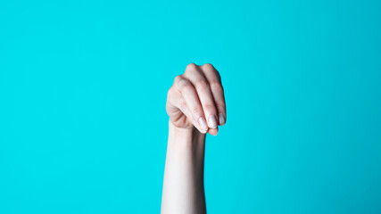 Beautiful Female Caucasian Hand in a Sprinkling Position. Fingers Pointing Downwards with a Simple Blue Background.