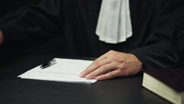 Male judge in black long robe signing papers, end of proceeding, justice