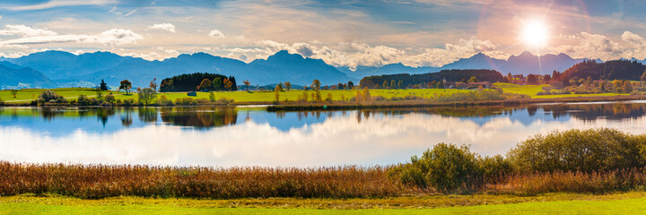 panoramic landscape in region Allgaeu with mountain range, lake and maedow