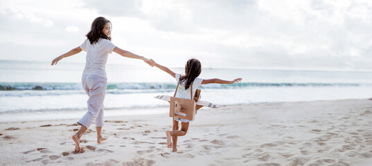 mother and daughter playing with cardboard airplane on the beach together