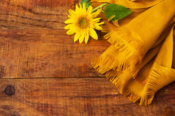 Flat composition with yellow knitted scarf and sunflower on a wooden table. Cozy autumn or the...