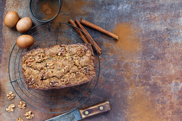 Top view of fresh homemade banana bread cooling on a baker's rack with ingredients nearby. Flatlay with copy space. Selective focus on loaf with blurred background