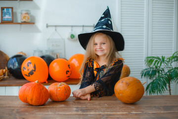 a little girl in a witch costume at home in the kitchen with pumpkins for halloween