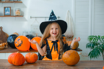 a little girl in a witch costume at home in the kitchen with pumpkins for halloween