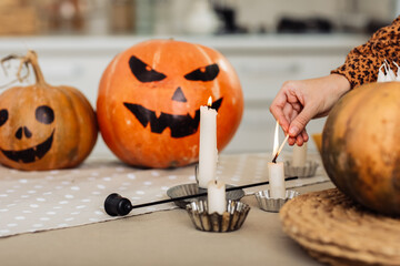 holidays and leisure concept - woman's hand with matches lighting candles at home on halloween....