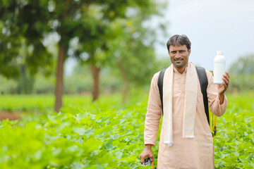 Young indian farmer showing liquid fertilizer bottle at agriculture field.