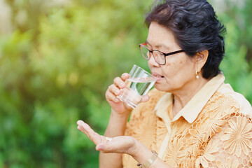 An old Thai woman sits and looks at the pill in her hand with a glass of water to eat and relieve...