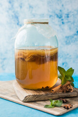 Raw fermented homemade alcoholic or non alcogolic kombucha superfood. Ice tea with healthy natural probiotic in glass with mint on  blue background