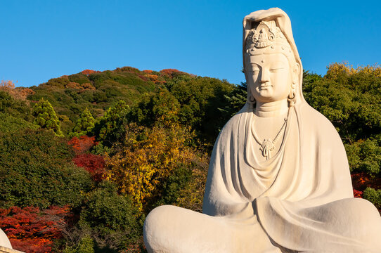 Giant statue of Ryozen Kannon Bodhisattva Avalokitesvara, illuminated by amazing sunlight, autumn mountains, blue sky.