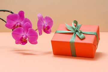 Red orchid flowers with gift box on a beige background.