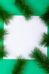 Composition of white card with copy space framed with fir tree branches on green background