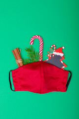 Composition of red face mask with christmas decorations on green background